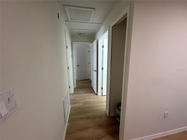 hallway featuring light wood finished floors, attic access, and baseboards