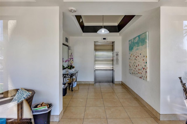 hall with baseboards, visible vents, elevator, light tile patterned flooring, and a raised ceiling