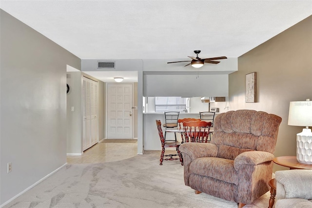 living area with visible vents, baseboards, light colored carpet, a textured ceiling, and a ceiling fan