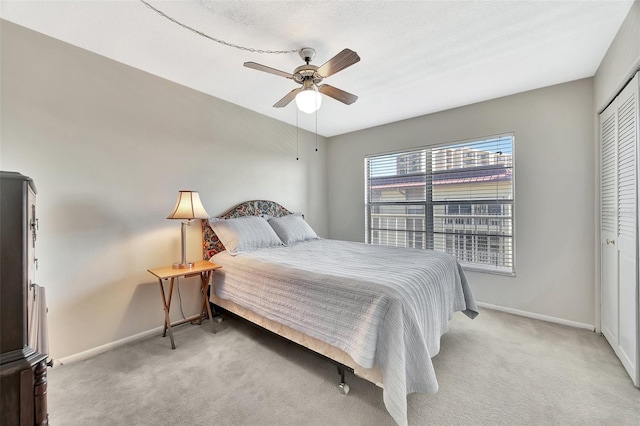 bedroom with a closet, light colored carpet, baseboards, and ceiling fan