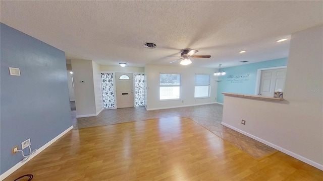 unfurnished living room with baseboards, visible vents, wood finished floors, a textured ceiling, and ceiling fan with notable chandelier