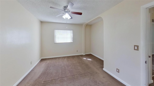 carpeted spare room with ceiling fan, baseboards, arched walkways, and a textured ceiling