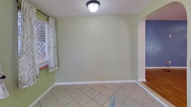 tiled empty room featuring baseboards, arched walkways, and a textured ceiling