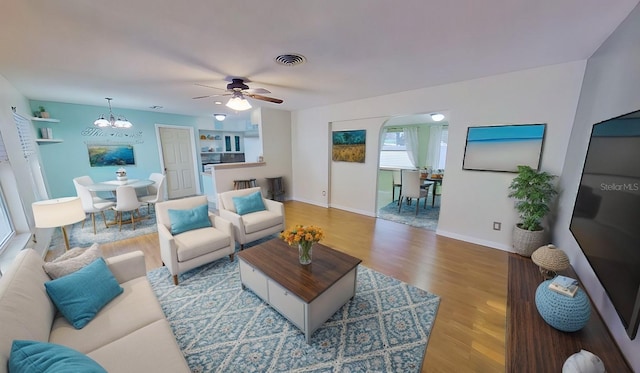 living area featuring baseboards, visible vents, wood finished floors, and ceiling fan with notable chandelier