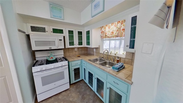 kitchen with tile countertops, backsplash, white cabinetry, a sink, and white appliances