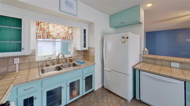 kitchen featuring tile countertops, white appliances, a sink, blue cabinetry, and backsplash