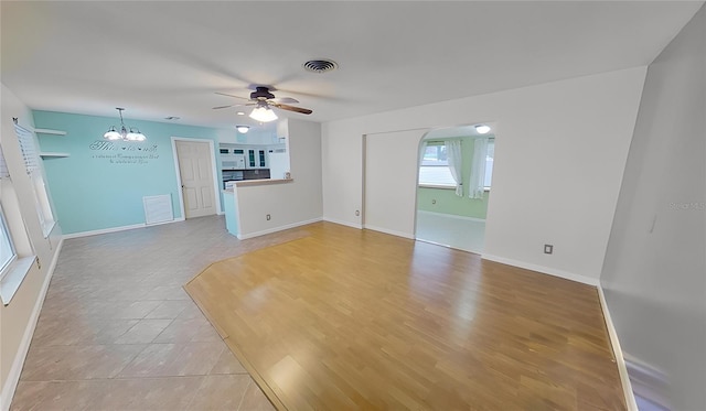 unfurnished living room featuring light tile patterned flooring, baseboards, visible vents, and ceiling fan with notable chandelier