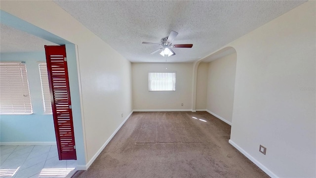 spare room featuring ceiling fan, a textured ceiling, arched walkways, and baseboards