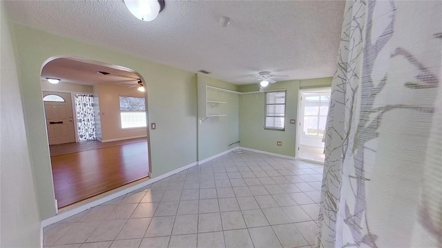 unfurnished room featuring arched walkways, ceiling fan, light tile patterned floors, and plenty of natural light