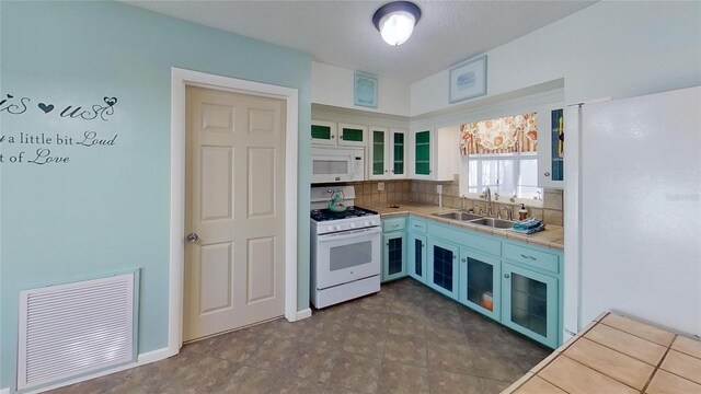 kitchen with white appliances, a sink, visible vents, white cabinetry, and glass insert cabinets