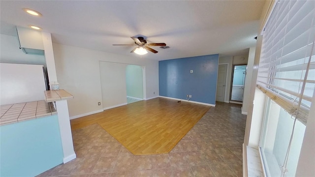 unfurnished living room featuring ceiling fan, baseboards, and tile patterned flooring