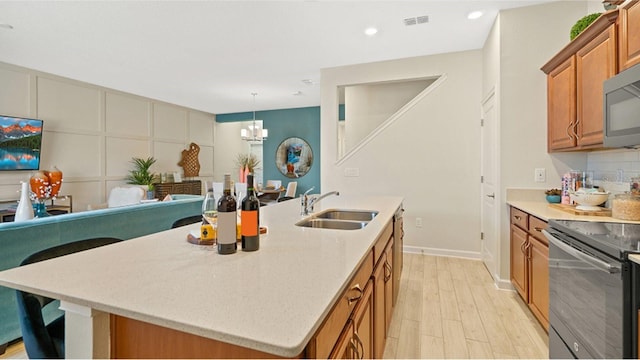 kitchen featuring black electric range oven, a sink, brown cabinets, stainless steel microwave, and an island with sink