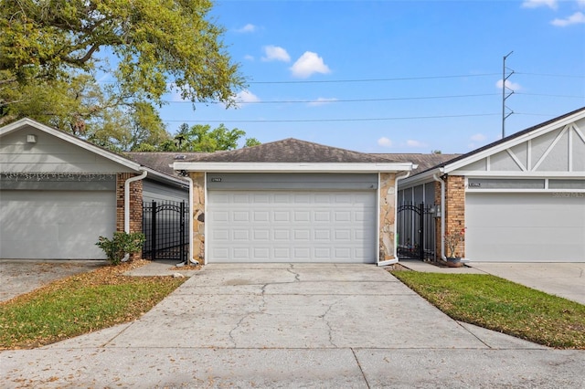 ranch-style house with concrete driveway, a gate, brick siding, and roof with shingles