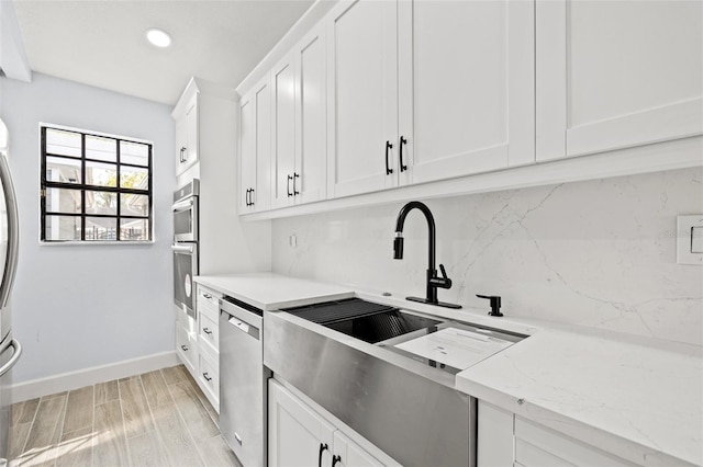 kitchen with baseboards, light wood finished floors, white cabinets, appliances with stainless steel finishes, and tasteful backsplash