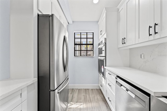 kitchen with baseboards, wood tiled floor, appliances with stainless steel finishes, white cabinetry, and tasteful backsplash