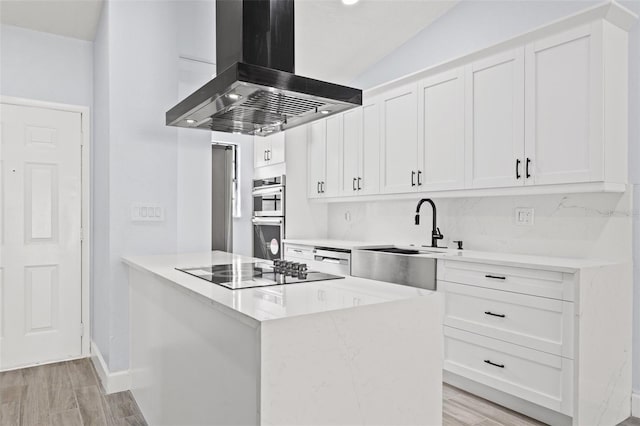 kitchen featuring stainless steel double oven, island exhaust hood, a sink, white cabinetry, and black electric cooktop