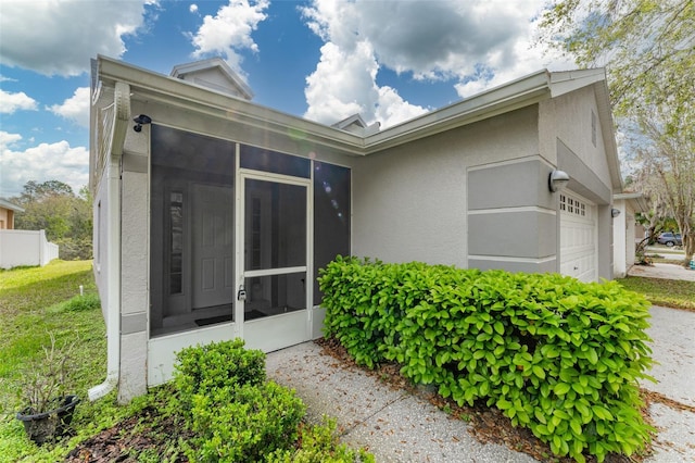 view of side of property featuring a garage, a sunroom, and stucco siding