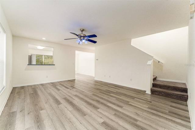 unfurnished living room featuring light wood finished floors, ceiling fan, stairs, and baseboards