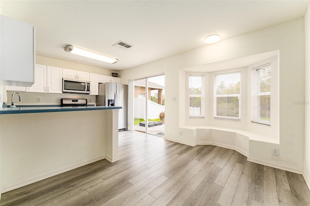 kitchen with stainless steel appliances, wood finished floors, visible vents, white cabinetry, and dark countertops