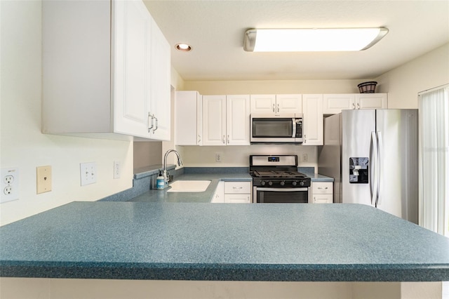 kitchen with a peninsula, a sink, white cabinetry, appliances with stainless steel finishes, and dark countertops