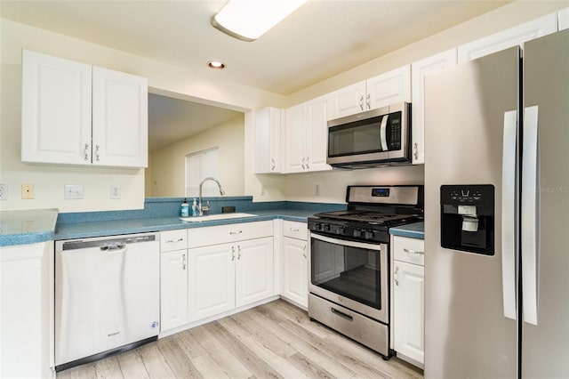 kitchen with white cabinets, dark countertops, appliances with stainless steel finishes, light wood-type flooring, and a sink