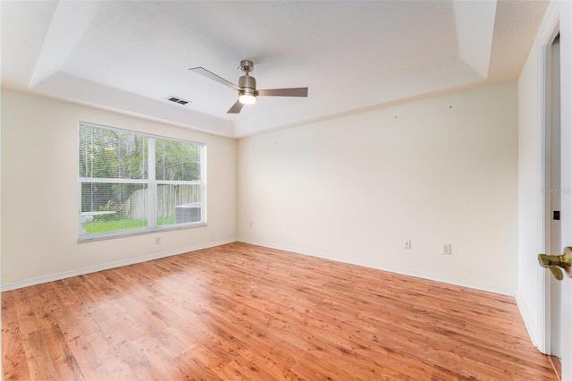 unfurnished room with a raised ceiling, light wood-style flooring, and baseboards