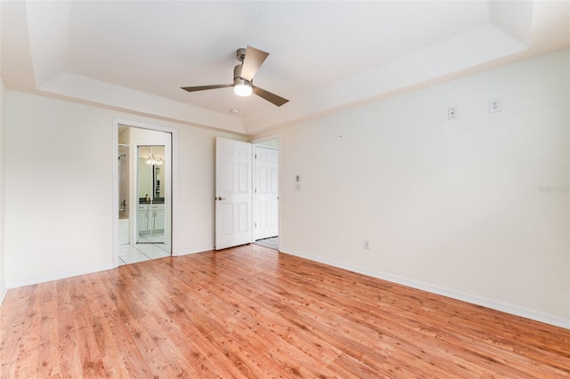 unfurnished room featuring a ceiling fan, a raised ceiling, light wood-style flooring, and baseboards