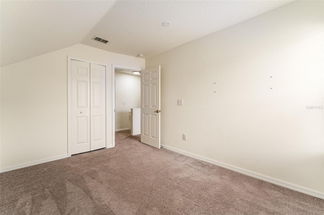 unfurnished bedroom with a closet, visible vents, carpet flooring, vaulted ceiling, and baseboards