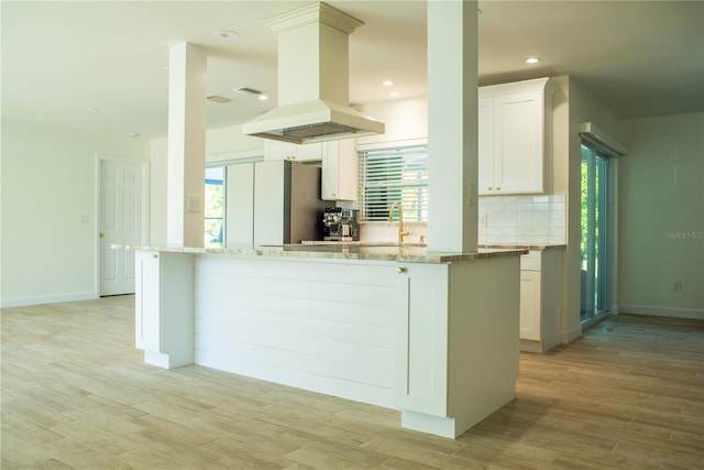 kitchen with light wood-type flooring, freestanding refrigerator, decorative backsplash, and island range hood