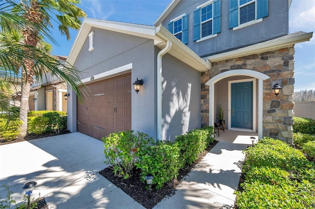 view of exterior entry with stone siding, concrete driveway, and stucco siding