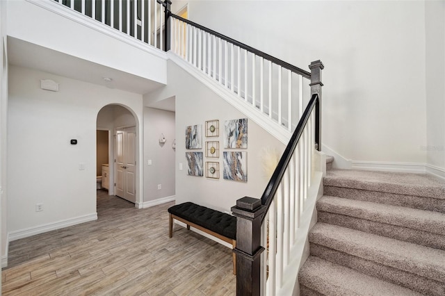 stairway with arched walkways, a towering ceiling, baseboards, and wood finished floors