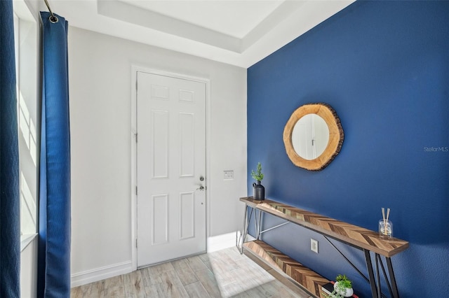 foyer with a raised ceiling, baseboards, and wood finished floors