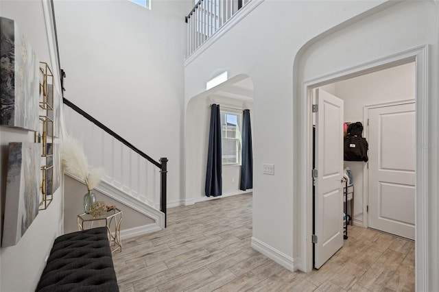 interior space with baseboards, arched walkways, a towering ceiling, stairway, and wood finished floors