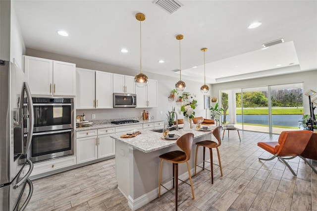 kitchen with stainless steel appliances, a tray ceiling, visible vents, and wood finish floors