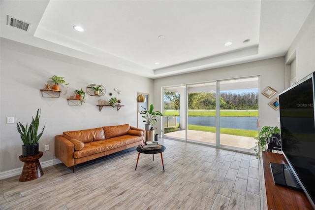 living room with light wood-type flooring, visible vents, and a tray ceiling