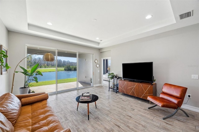 living area featuring light wood-type flooring, a raised ceiling, and visible vents