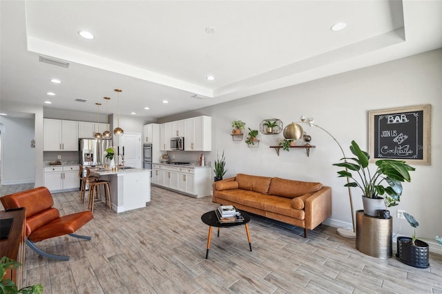 living area featuring a tray ceiling, visible vents, and wood tiled floor