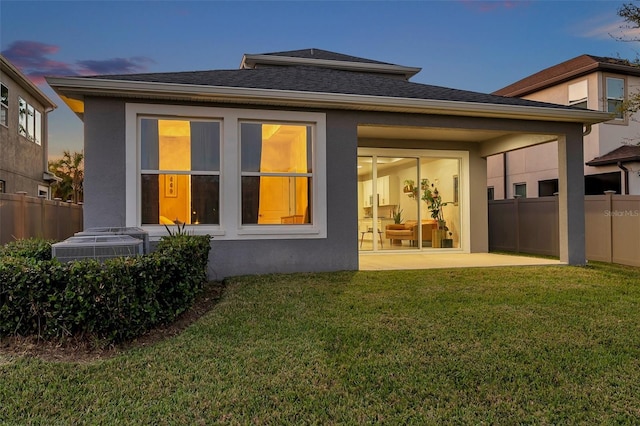 rear view of property with a shingled roof, fence, a lawn, and stucco siding