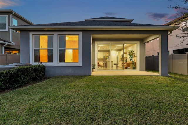 rear view of house with stucco siding, fence, and a yard