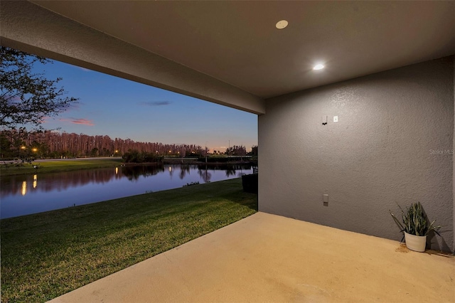 patio terrace at dusk featuring a water view and a yard