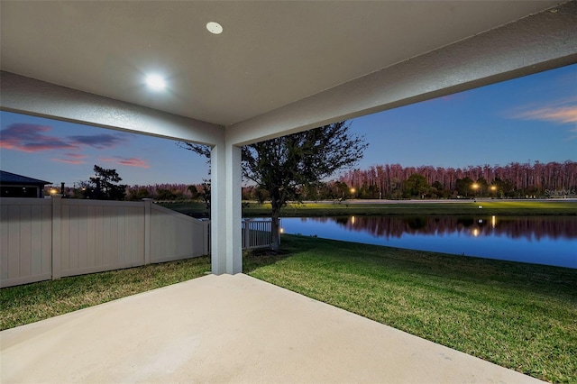 patio terrace at dusk with a water view, fence, and a yard