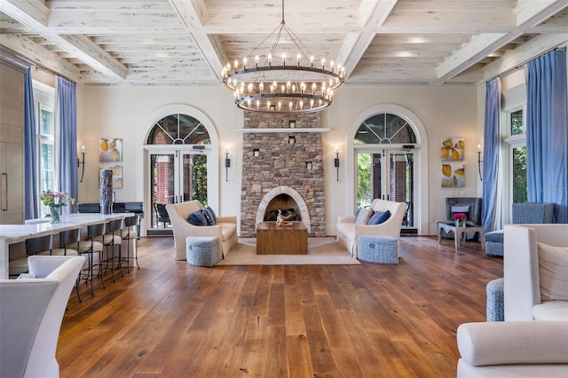 living area with wood-type flooring, coffered ceiling, a stone fireplace, and beam ceiling