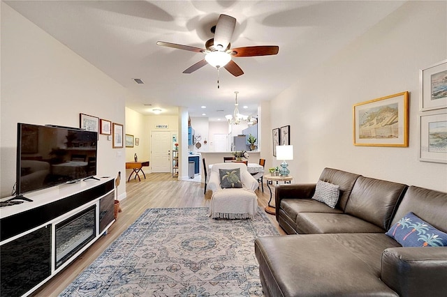 living area with visible vents, light wood-style flooring, and ceiling fan with notable chandelier