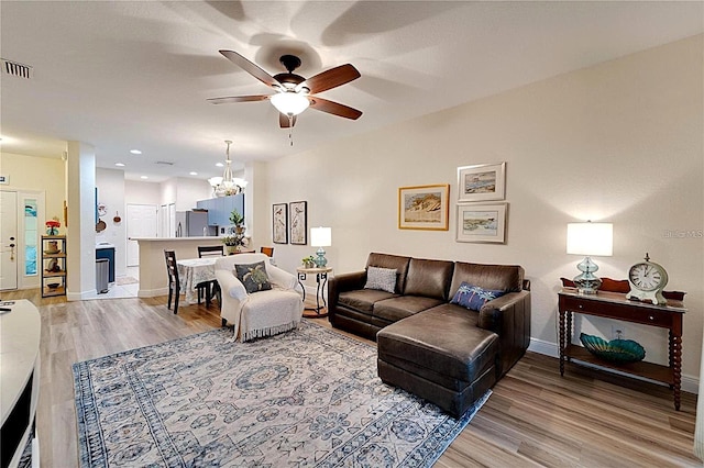 living area with visible vents, ceiling fan with notable chandelier, baseboards, and light wood finished floors