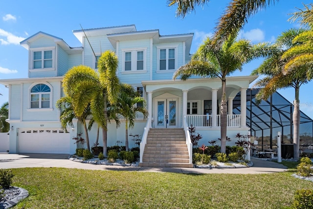 beach home with stairway, driveway, a porch, an attached garage, and a front lawn