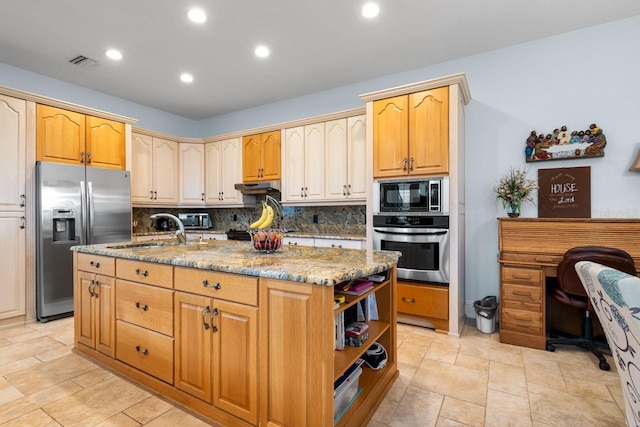 kitchen with a sink, light stone countertops, under cabinet range hood, appliances with stainless steel finishes, and a kitchen island with sink