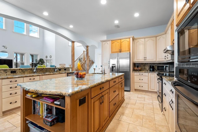 kitchen with light stone countertops, an island with sink, decorative backsplash, arched walkways, and stainless steel appliances