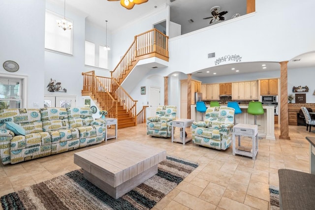 living room with visible vents, stairs, ceiling fan with notable chandelier, arched walkways, and ornate columns