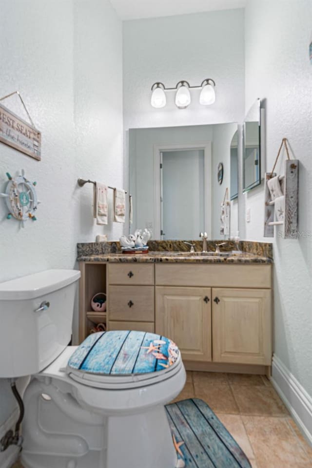 bathroom featuring vanity, baseboards, tile patterned flooring, toilet, and a textured wall