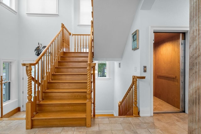 stairs featuring baseboards, elevator, and a towering ceiling